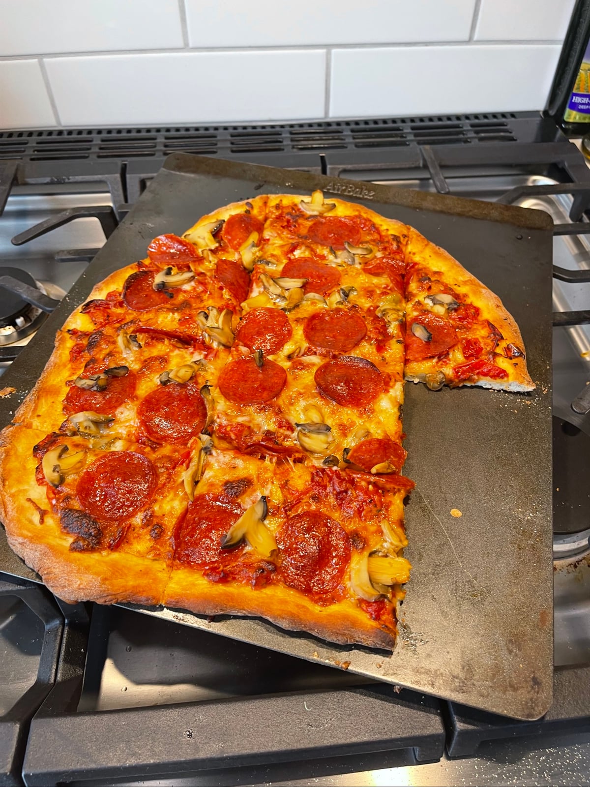 Baked pizza with pepperoni and yellow peppers on a pizza stone, on stovetop.